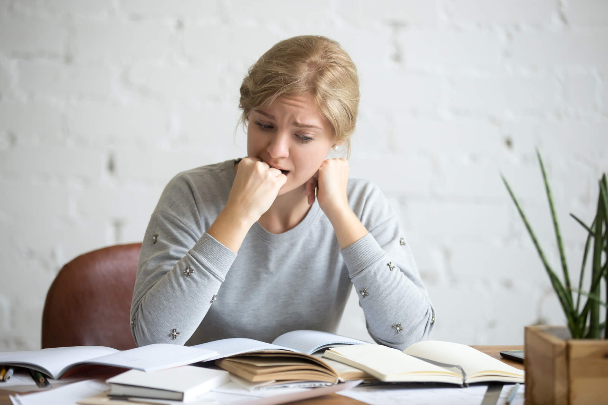 Portrait of a student girl sitting at the desk biting her fist