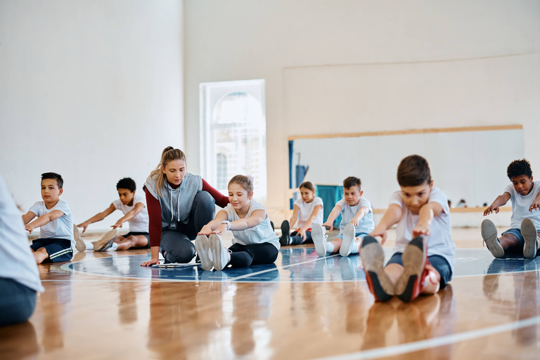 Young coach and group of kids on physical education class at school gymnasium.