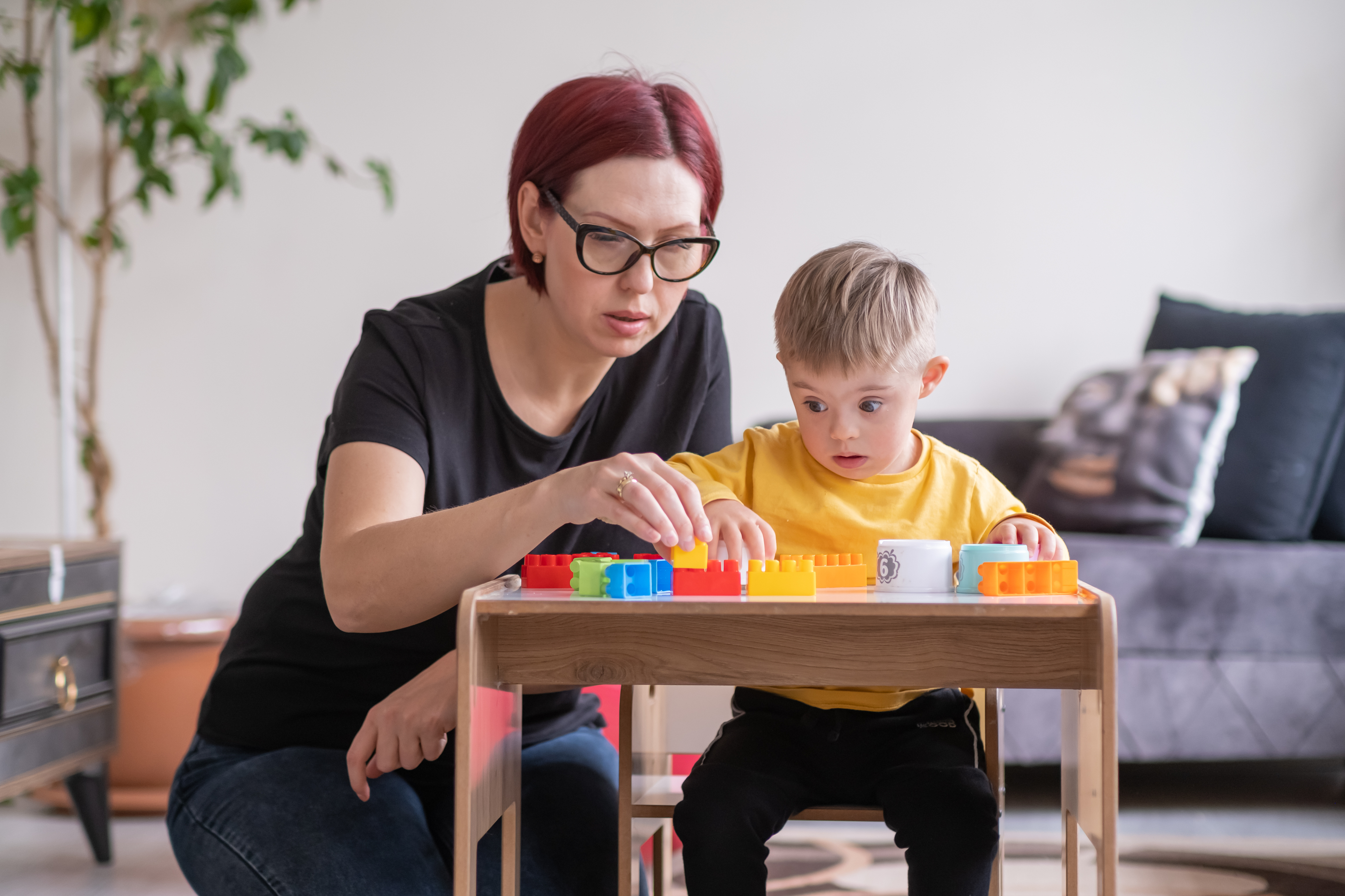 child living with Down syndrome learning and playing with educational toys, supported by his mom